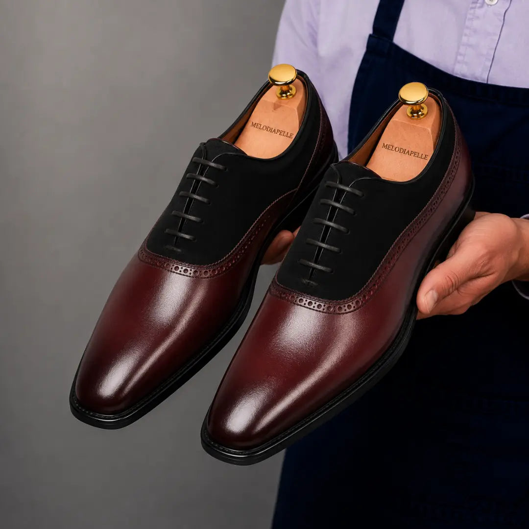 Man holding a pair of Melodiapelle Bellagio Oxford shoes in burgundy leather and black suede, close-up