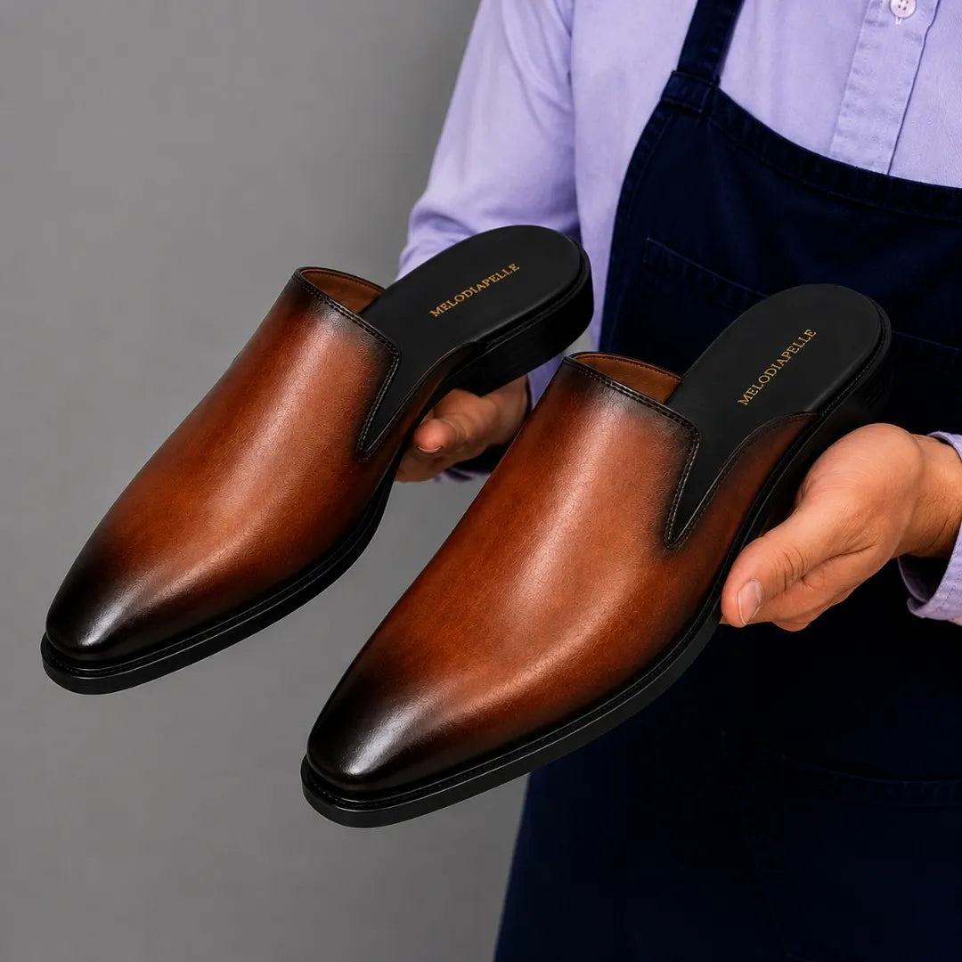 Man holding a pair of Melodiapelle Farida Mules in rust tan leather, close-up