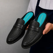 Man holding a pair of Melodiapelle Madana Mule shoes in black woven leather, close-up