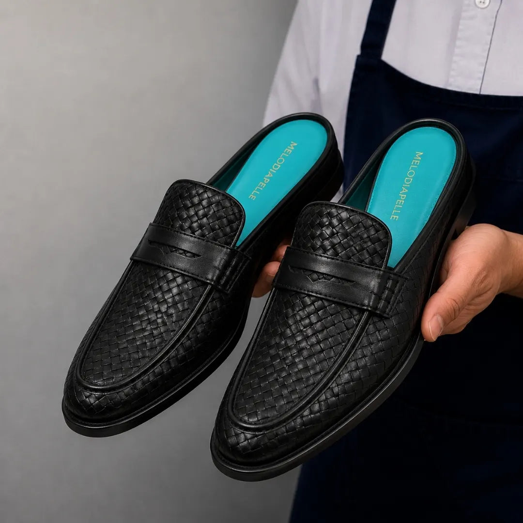 Man holding a pair of Melodiapelle Madana Mule shoes in black woven leather, close-up
