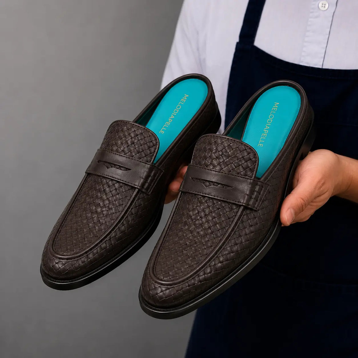 Man holding a pair of Melodiapelle Madana Mule shoes in dark brown woven leather, close-up