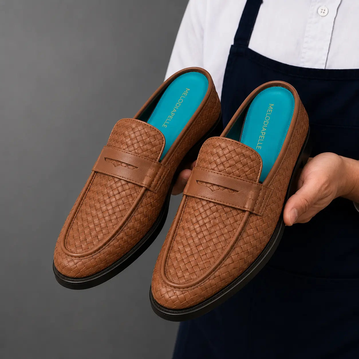 Man holding a pair of Melodiapelle Madana Mule shoes in tan woven leather, close-up