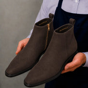 Man holding a pair of Melodiapelle Maddox Suede Zip Boots in brown suede, close-up