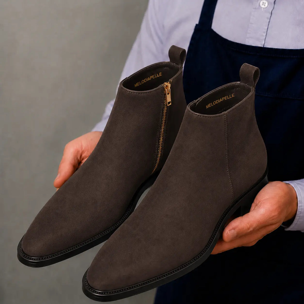 Man holding a pair of Melodiapelle Maddox Suede Zip Boots in brown suede, close-up