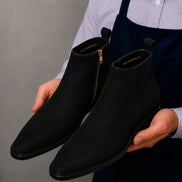 Man holding a pair of Melodiapelle Maddox Suede Zip Boots in black suede, close-up