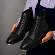 Man holding a pair of Melodiapelle Madison Combat Boots in black leather, close-up