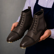 Man holding a pair of Melodiapelle Madison Combat Boots in dark brown leather, close-up