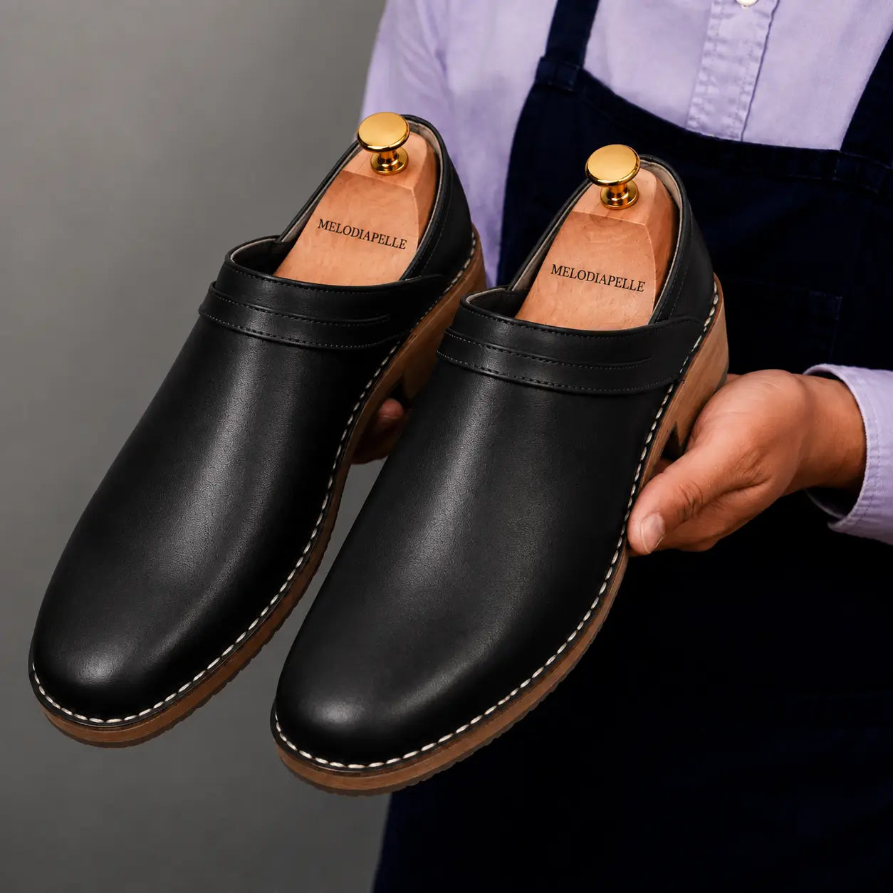Man holding a pair of Melodiapelle Madison Mules in black leather, close-up
