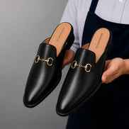 Man holding a pair of Melodiapelle Madison Mule shoes in black leather, close-up