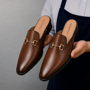 Man holding a pair of Melodiapelle Madison Mule shoes in brown leather, close-up