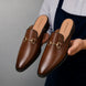 Man holding a pair of Melodiapelle Madison Mule shoes in brown leather, close-up