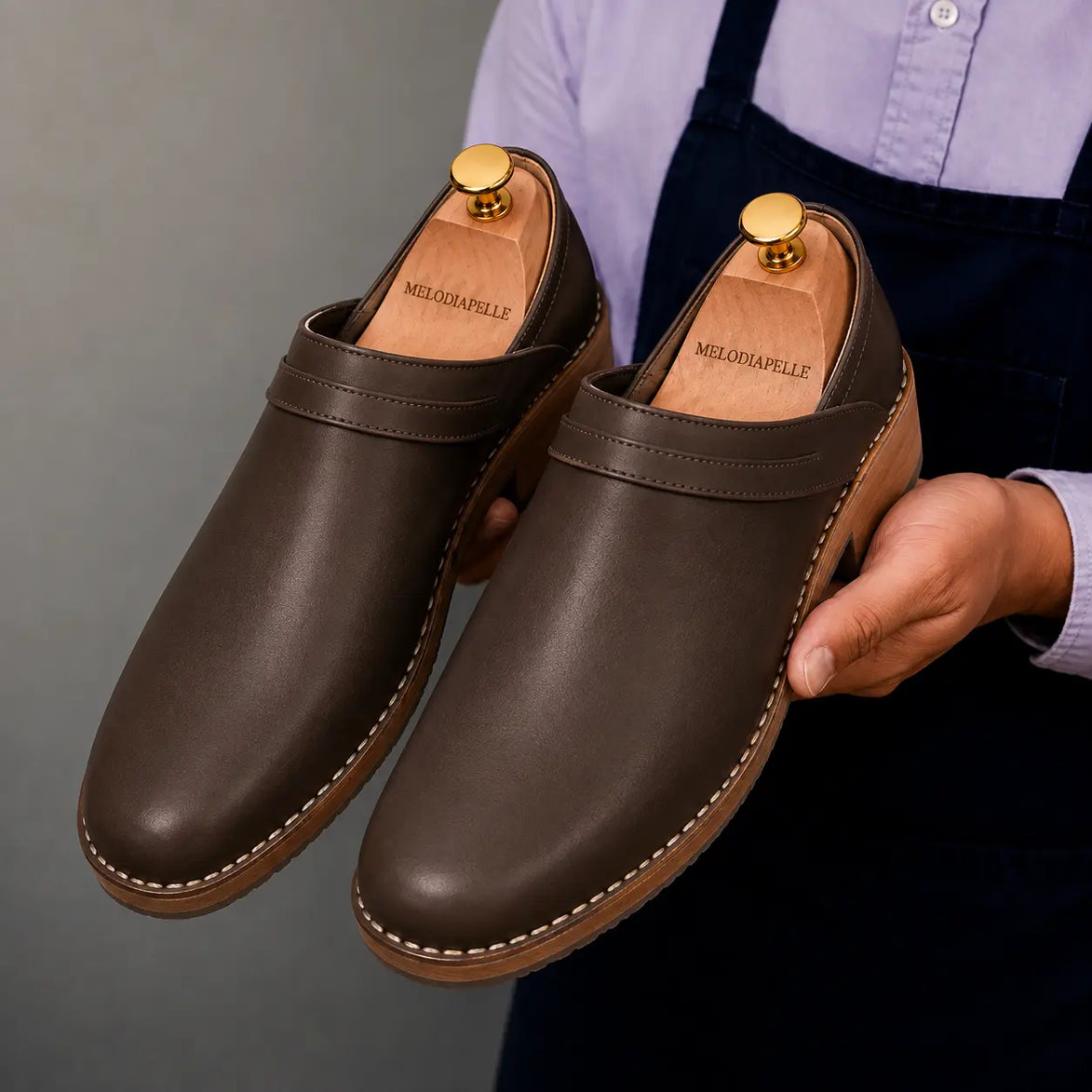 Man holding a pair of Melodiapelle Madison Mules in dark brown leather, close-up