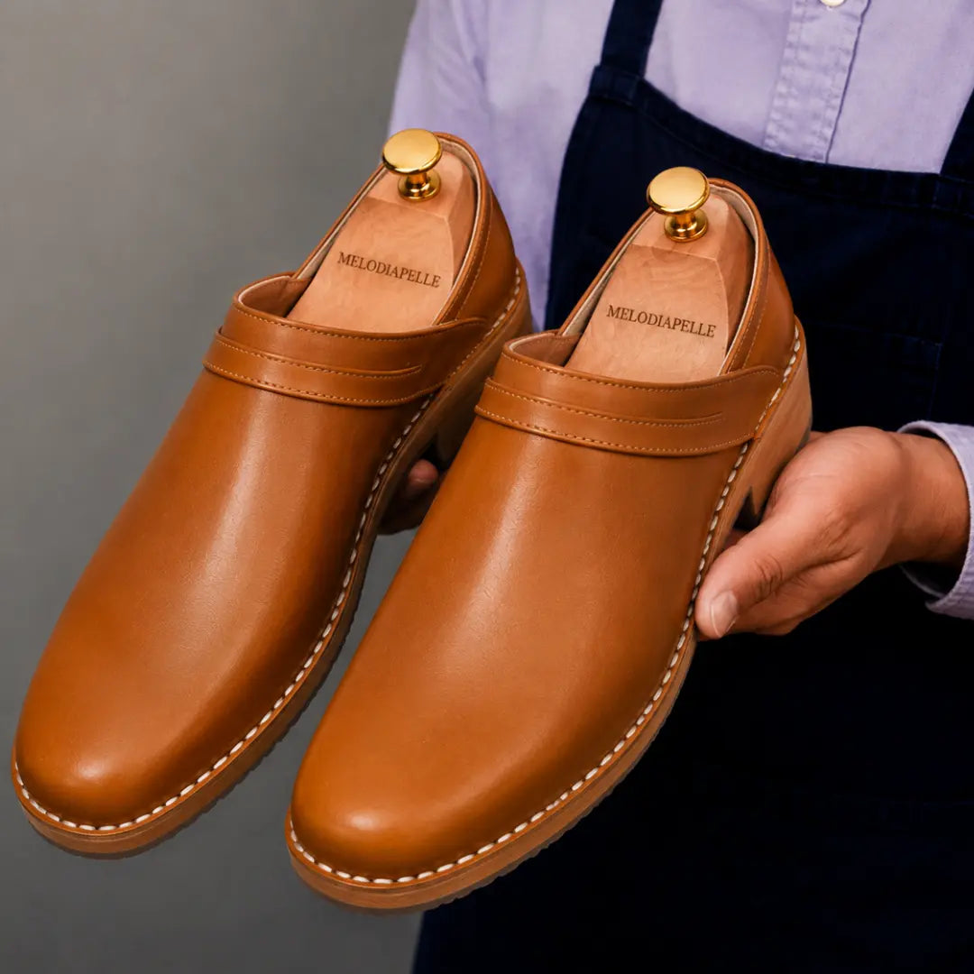 Man holding a pair of Melodiapelle Madison Mules in tan leather, close-up