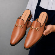 Man holding a pair of Melodiapelle Madison Mule shoes in tan leather, close-up