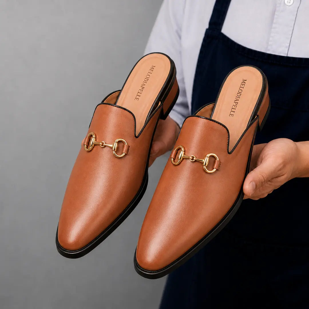 Man holding a pair of Melodiapelle Madison Mule shoes in tan leather, close-up