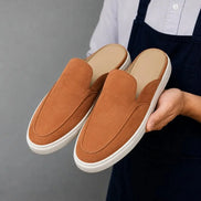 Man holding a pair of Melodiapelle Madurai Mule shoes in rust tan suede, close-up