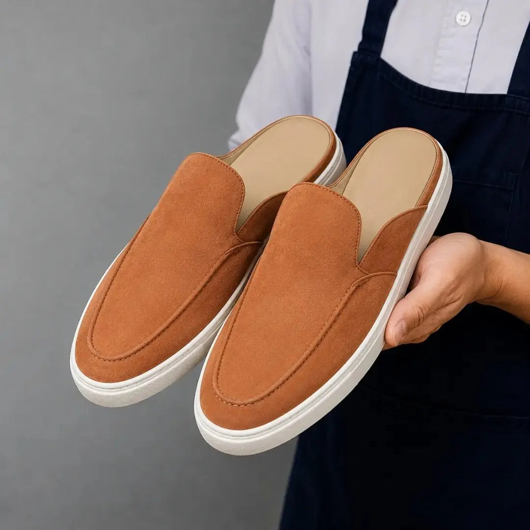Man holding a pair of Melodiapelle Madurai Mule shoes in rust tan suede, close-up