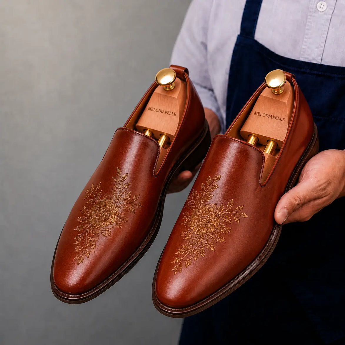Man holding a pair of Melodiapelle Maestro Embroidered Opera Loafers in cognac tan leather, close-up