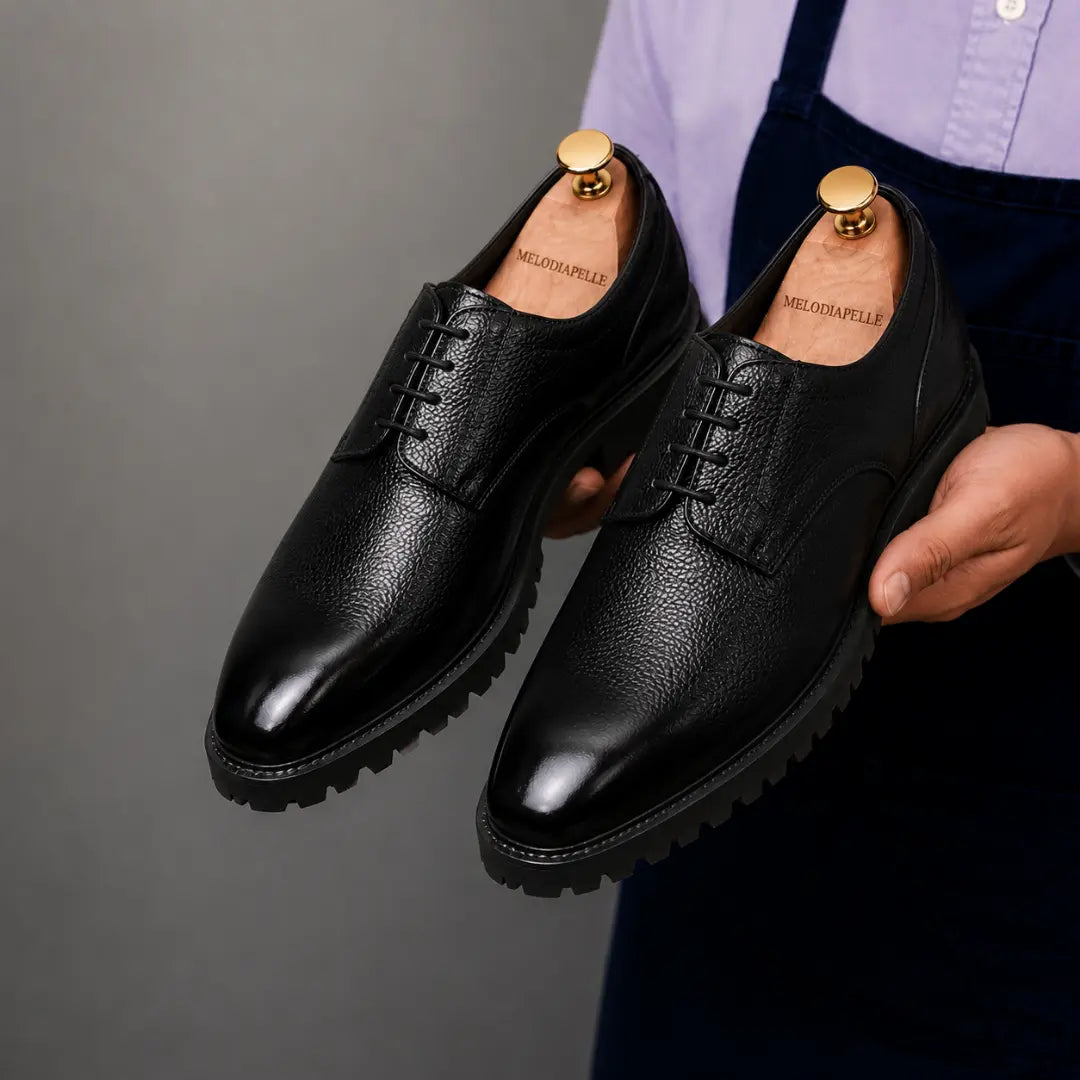 Man holding a pair of Melodiapelle Magnum Derby Shoes in black leather, close-up