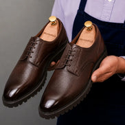 Man holding a pair of Melodiapelle Magnum Derby Shoes in dark brown leather, close-up