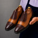 Man holding a pair of Melodiapelle Maiden Oxford Shoes in tan and dark brown leather, close-up