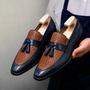 Man holding a pair of Melodiapelle Maison Woven Two-Tone Penny Loafer shoes in midnight navy and tan leather, close-up