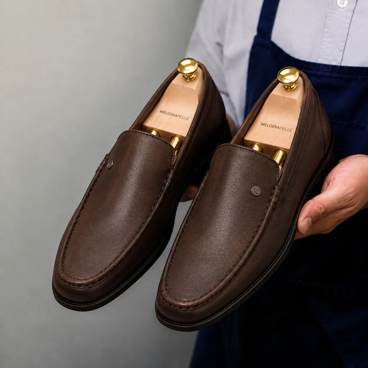 Man holding a pair of Melodiapelle Malaga Driving Loafers in dark chocolate leather, close-up