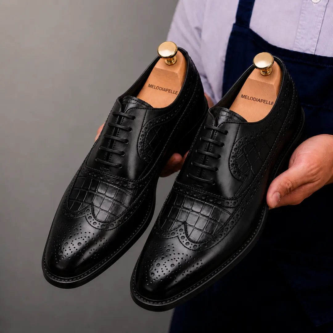 Man holding a pair of Melodiapelle Malcomb Croc-Panel Wingtip Derby shoes in black leather, close-up
