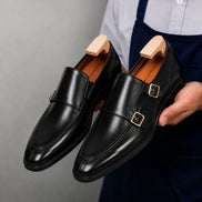 Man holding a pair of Melodiapelle Malibu Apron Monk Strap shoes in nero black leather, close-up