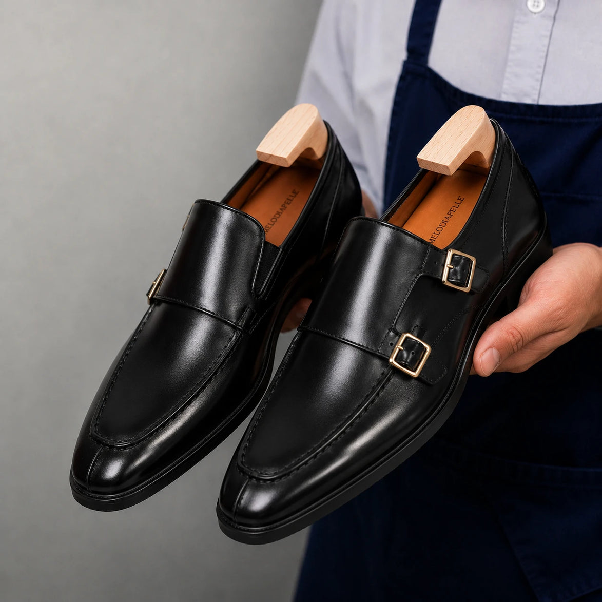 Man holding a pair of Melodiapelle Malibu Apron Monk Strap shoes in nero black leather, close-up