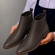 Man holding a pair of Melodiapelle Malone Zip Ankle Boots in dark brown leather, close-up
