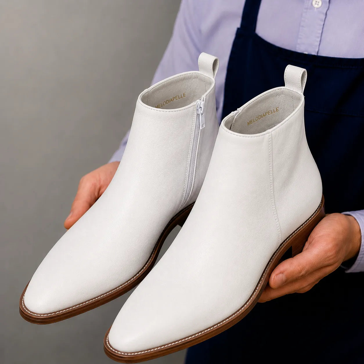Man holding a pair of Melodiapelle Malone Zip Ankle Boots in pearl white leather, close-up