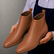 Man holding a pair of Melodiapelle Malone Zip Ankle Boots in tan leather, close-up