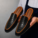 Man holding a pair of Melodiapelle Malta Mule shoes in black croc-embossed leather with orange piping, close-up