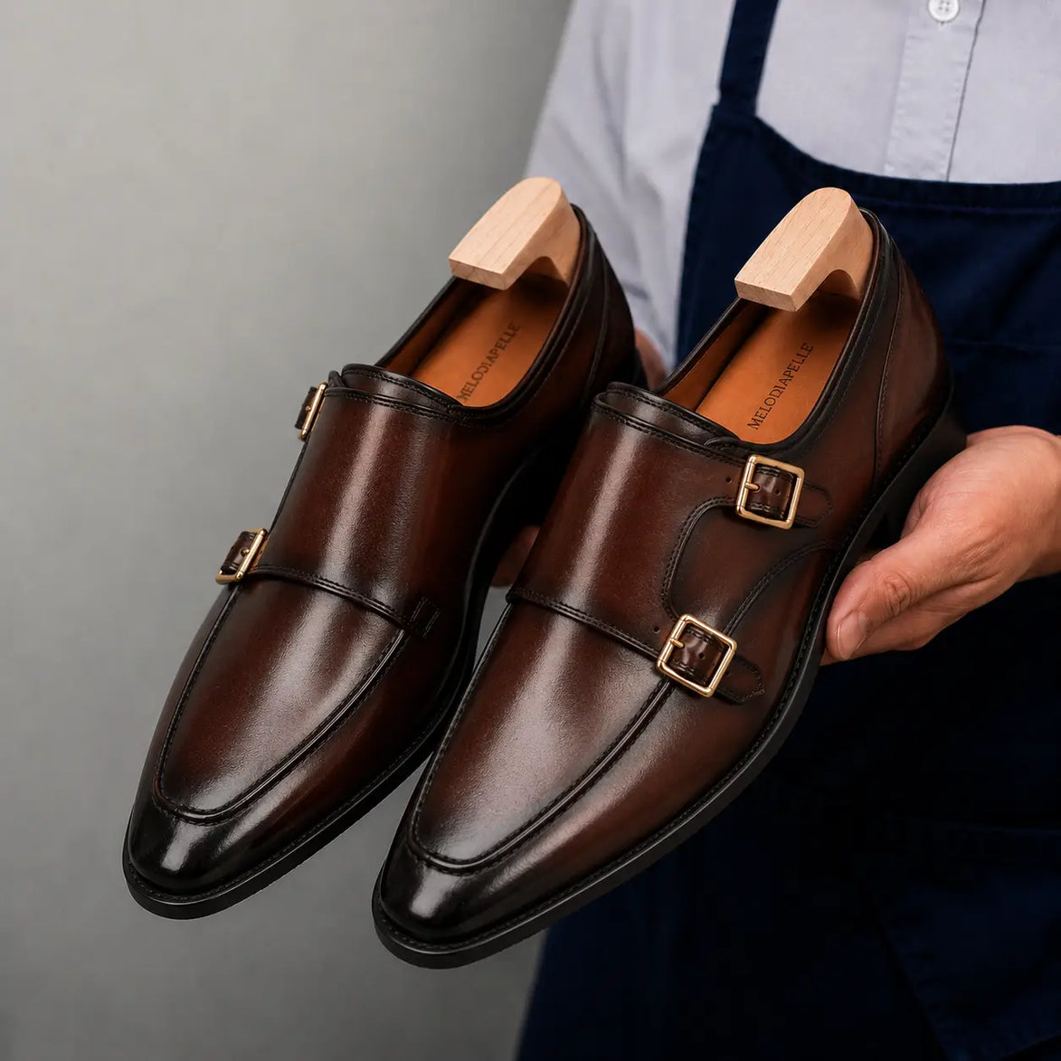 Man holding a pair of Melodiapelle Malvern Apron Monk Strap shoes in dark mahogany leather, close-up