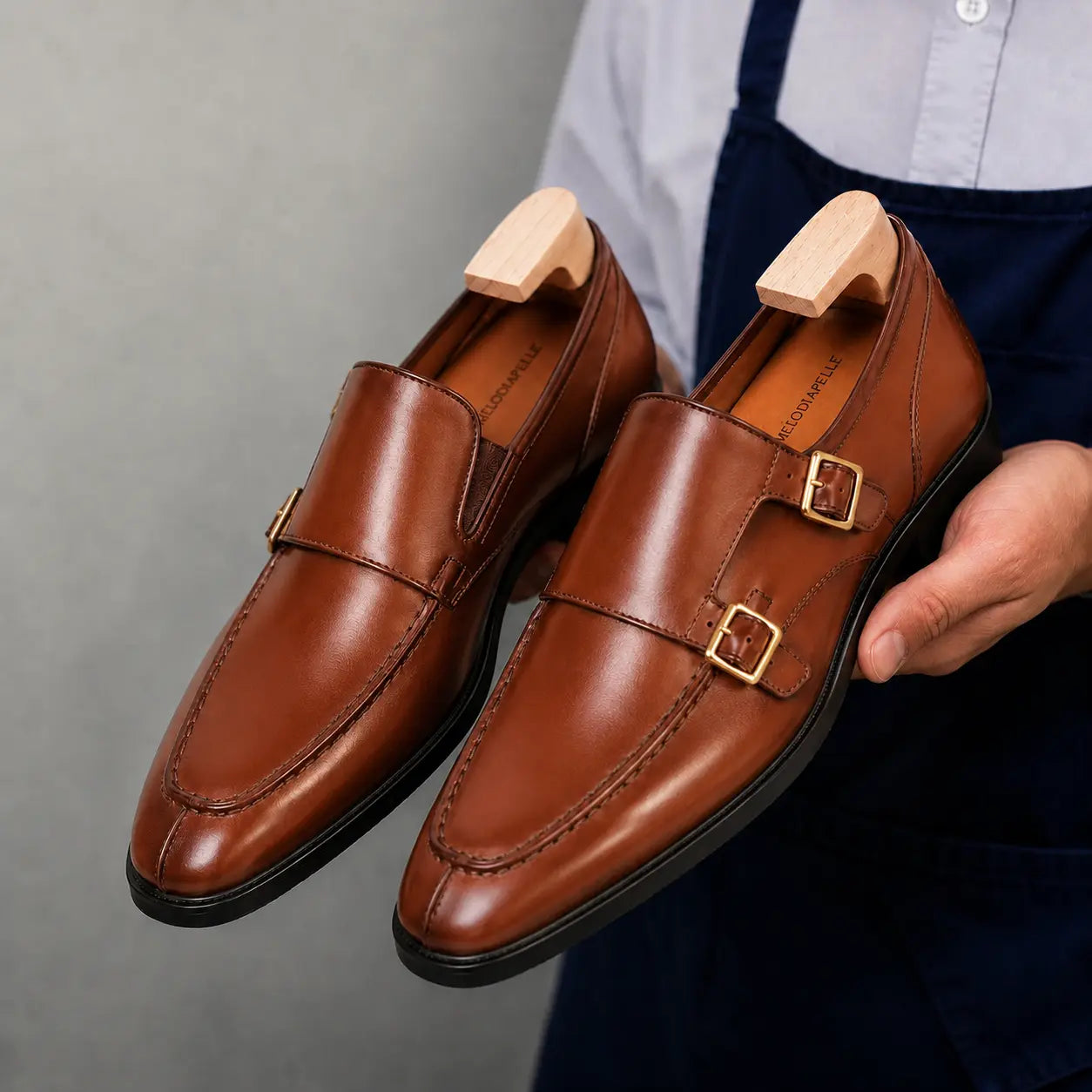 Man holding a pair of Melodiapelle Malvern Apron Monk Strap shoes in tan leather, close-up