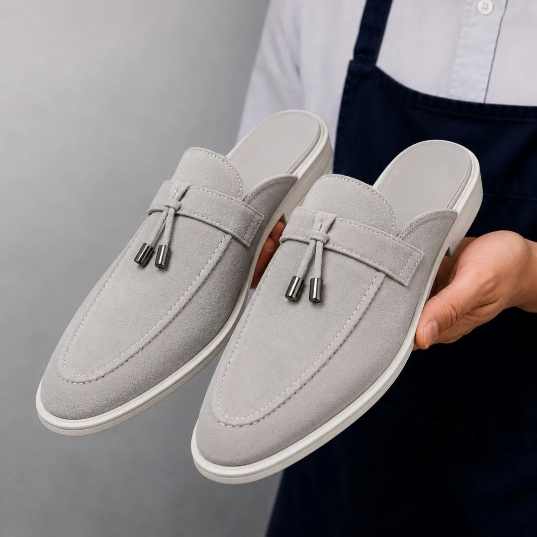 Man holding a pair of Melodiapelle Mandelli Mule shoes in light grey suede, close-up