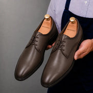 Man holding a pair of Melodiapelle Mangrove Plain Derby shoes in brown leather, close-up