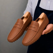 Man holding a pair of Melodiapelle Manhattan Loafers in rust tan leather, close-up