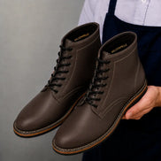 Man holding a pair of Melodiapelle Manila Plain Toe Boots in brown leather, close-up