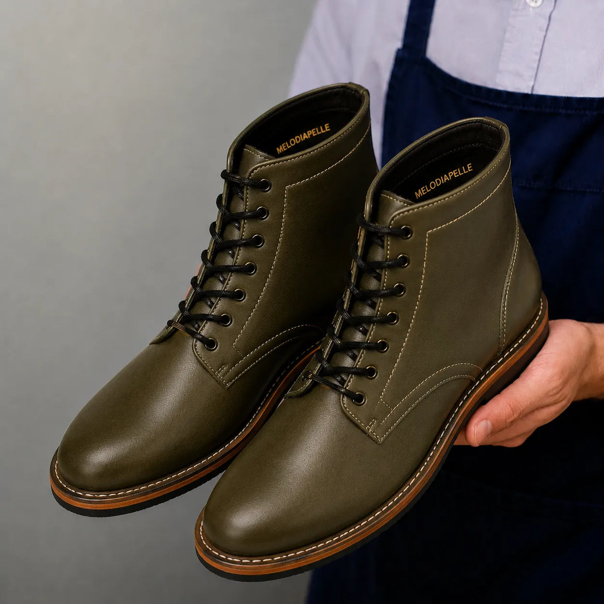 Man holding a pair of Melodiapelle Manila Plain Toe Boots in olive green leather, close-up