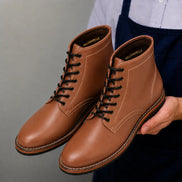Man holding a pair of Melodiapelle Manila Plain Toe Boots in tan leather, close-up