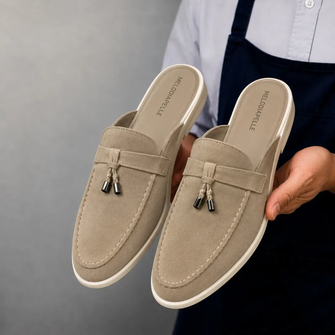 Man holding a pair of Melodiapelle Manni Mule shoes in sand beige suede, close-up