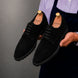 Man holding a pair of Melodiapelle Mansfield Classy Derby shoes in black suede, close-up
