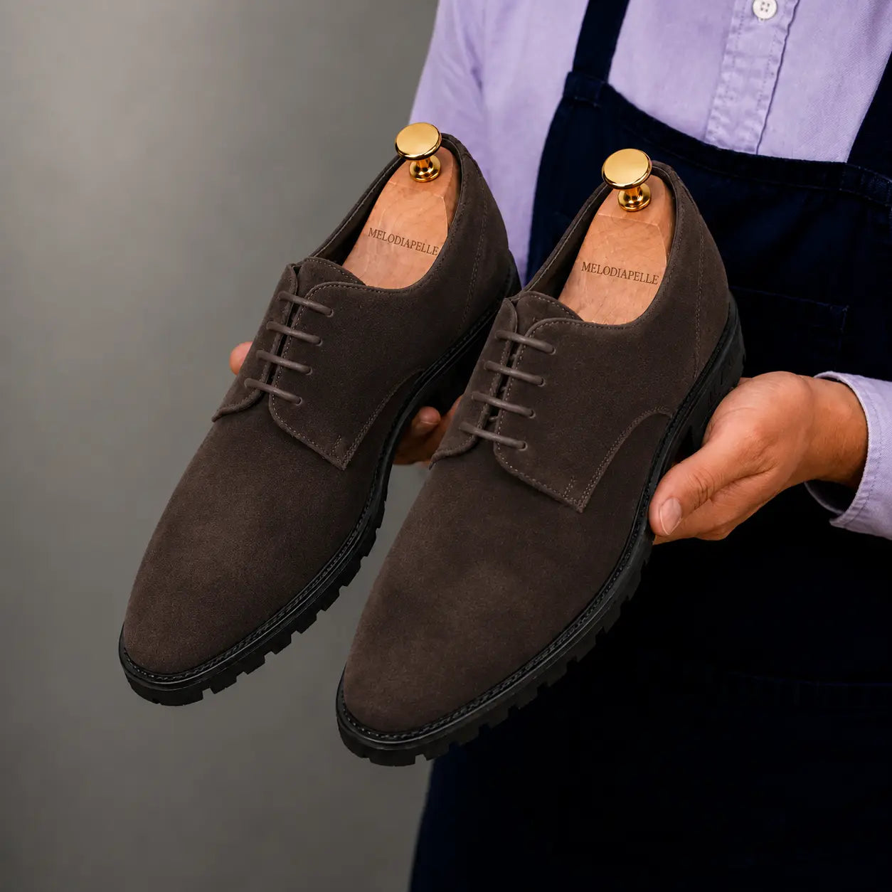 Man holding a pair of Melodiapelle Mansfield Classy Derby shoes in dark brown suede, close-up