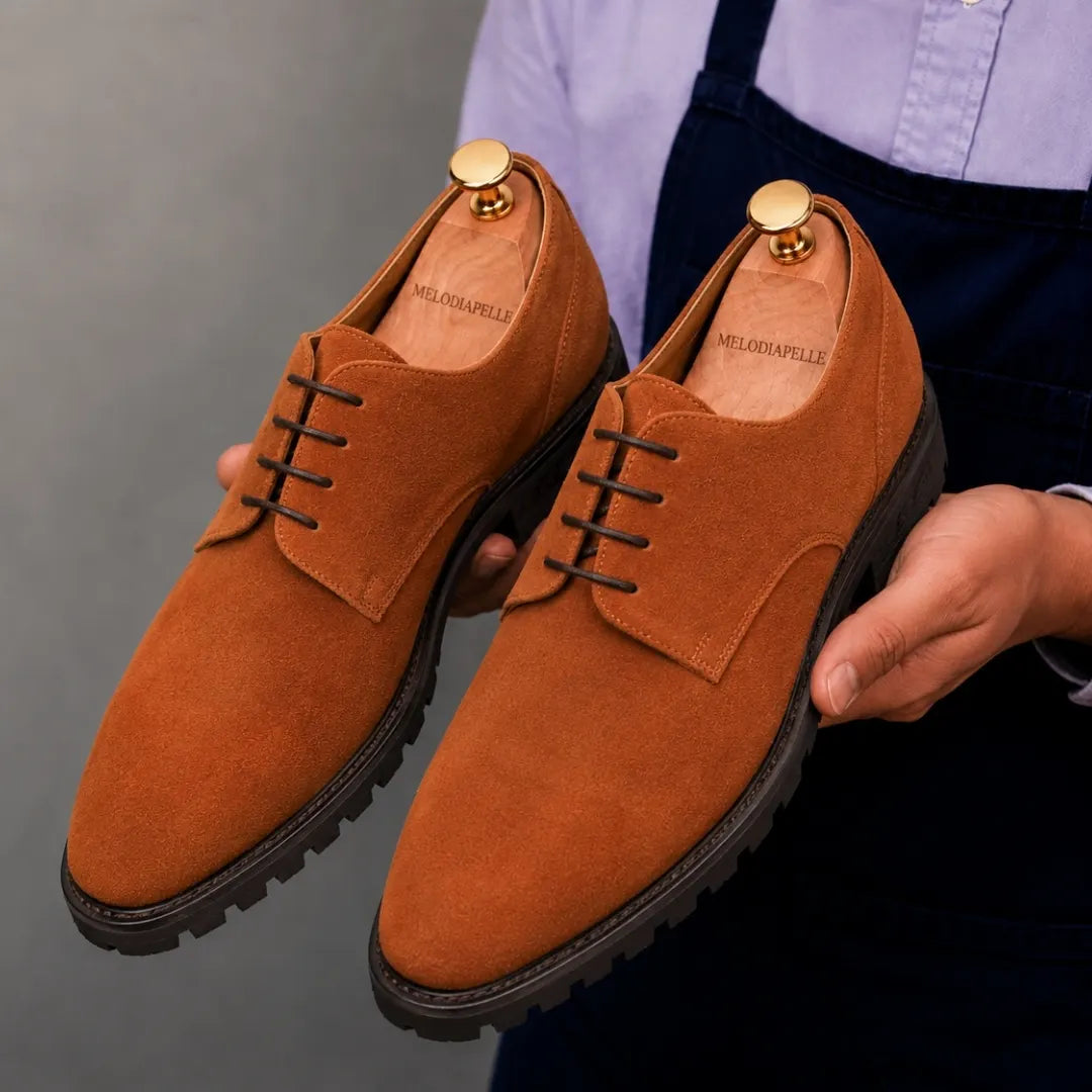Man holding a pair of Melodiapelle Mansfield Classy Derby shoes in rust tan suede, close-up
