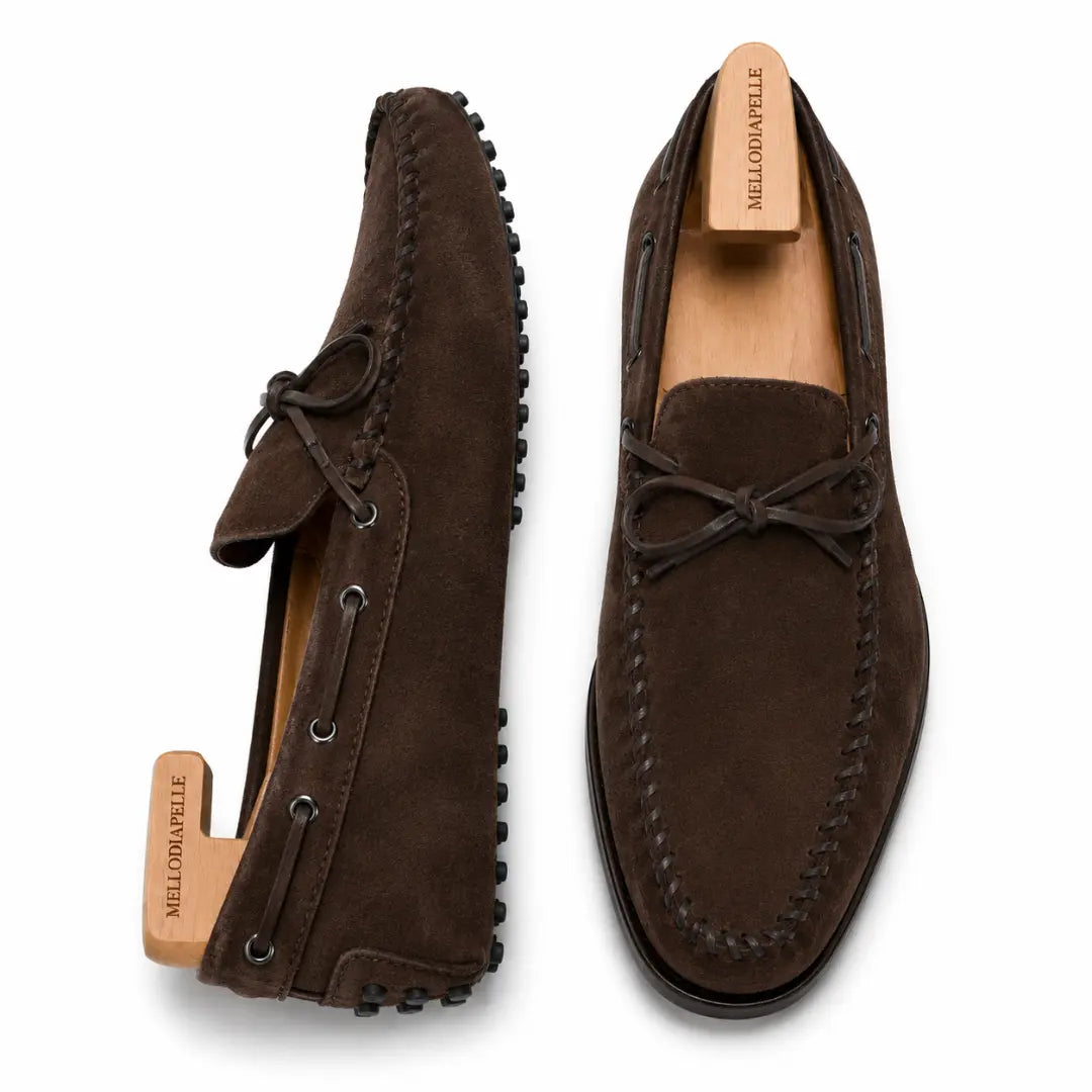 Dark brown suede driving loafer with bow lace, three-quarter angle showing sole detailing