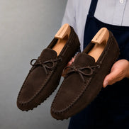 Man holding a pair of Melodiapelle Mansfield Loafers in dark brown suede, close-up