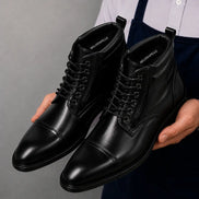 Man holding a pair of Melodiapelle Manteca Combat Boots in black leather, close-up