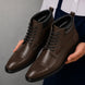 Man holding a pair of Melodiapelle Manteca Combat Boots in dark brown leather, close-up